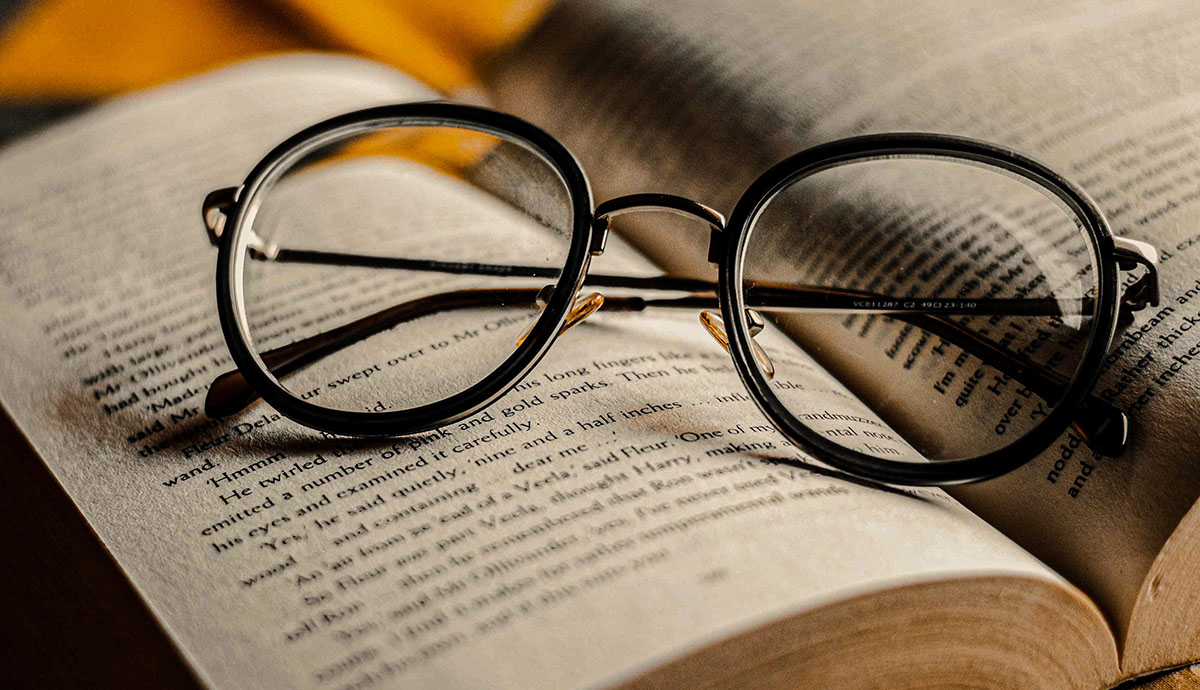 Header Graphic: A pair of black glasses resting right side up atop an open book | Image Credit: Jackson Films via Unsplash