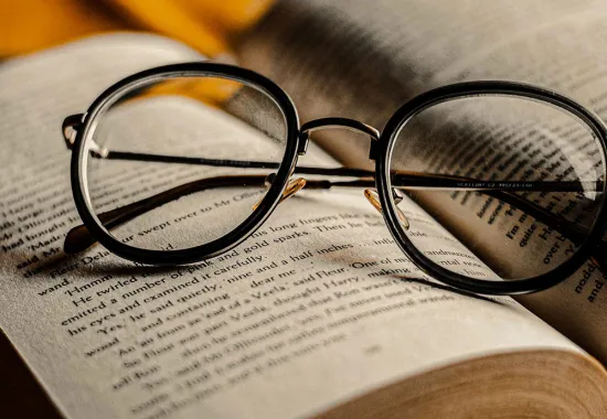 Header Graphic: A pair of black glasses resting right side up atop an open book | Image Credit: Jackson Films via Unsplash