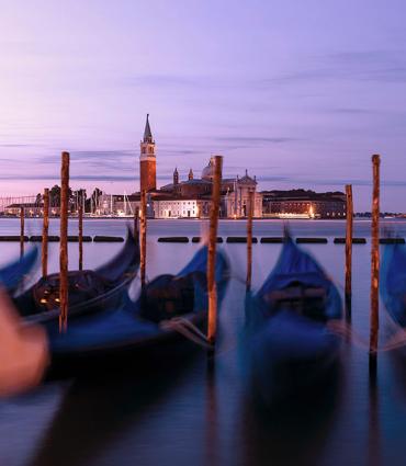 Blurry image of gondolas docked on a body of water in Italy in the evening | Image Credit: Geoffroy Hauwen via Unsplash