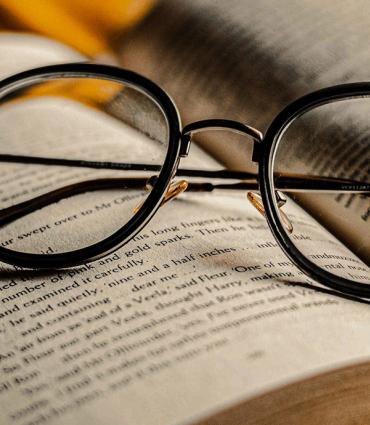 Header Graphic: A pair of black glasses resting right side up atop an open book | Image Credit: Jackson Films via Unsplash