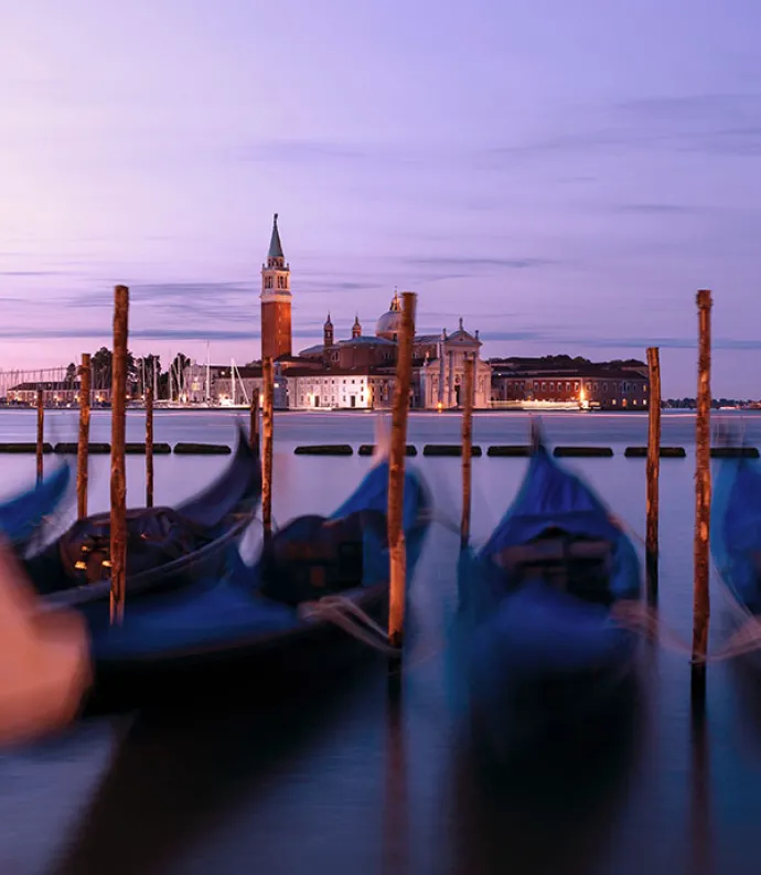 Blurry image of gondolas docked on a body of water in Italy in the evening | Image Credit: Geoffroy Hauwen via Unsplash