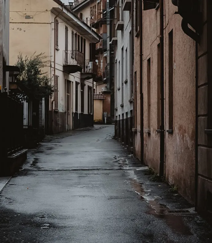 Header Graphic: dark and rainy street tunneled by tan buildings and copper brick buildings that curve right into the crowded distance| Image Credit: Unsplash